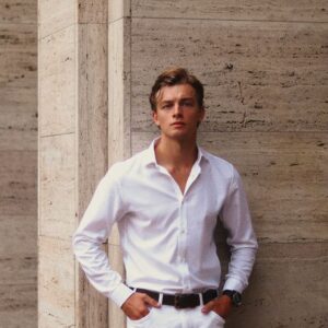 A young man in a white shirt leans against a modern architectural wall.