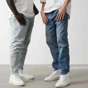 Close-up of two individuals wearing jeans and white sneakers in a minimalist setting.