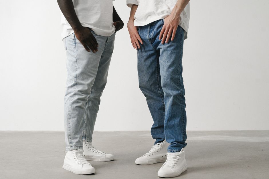 Close-up of two individuals wearing jeans and white sneakers in a minimalist setting.